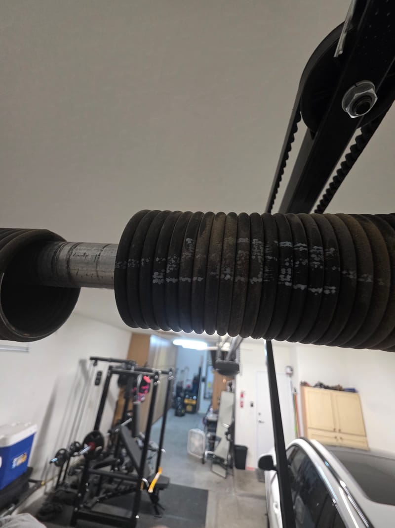Garage door torsion spring and belt drive seen from below, with a garage in the background